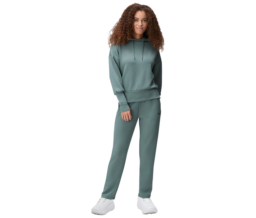 Jeune femme aux cheveux bruns bouclés portant un survêtement vert et des baskets blanches.