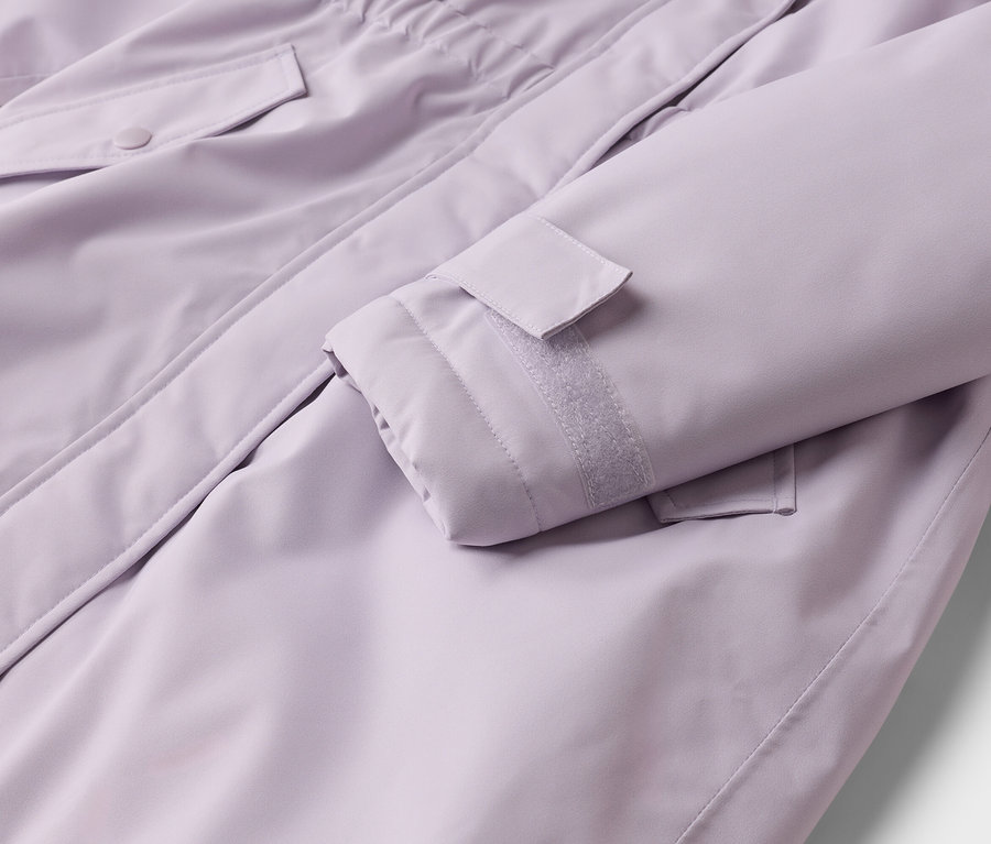 Gros plan d'une veste lilas, montrant une manche avec un poignet réglable à scratch et une poche à rabat boutonnée.