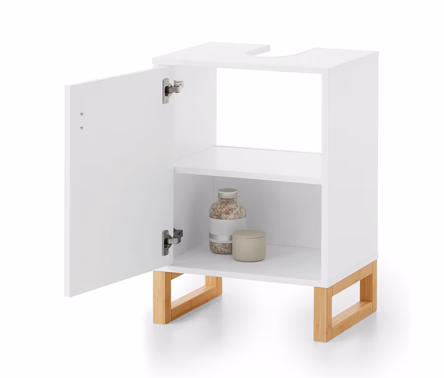 Meuble de salle de bain blanc avec sa porte gauche ouverte. Il présente une découpe en U sur le dessus, une étagère intérieure et des pieds en bois clair. Sur l'étagère inférieure se trouvent une bouteille de sels de bain et un petit pot avec couvercle.