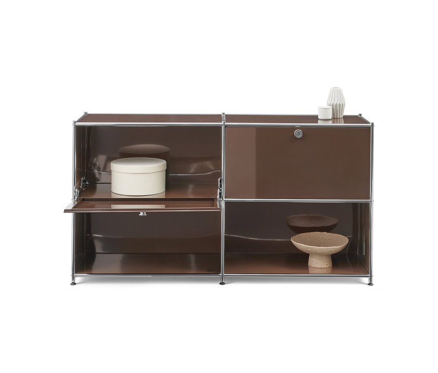 Un meuble modulaire marron avec des cadres chromés. Le côté gauche a une étagère supérieure ouverte avec une boîte ronde blanche et une porte inférieure partiellement ouverte. Le côté droit a une porte supérieure fermée et une étagère inférieure ouverte présentant deux bols décoratifs. Deux objets décoratifs blancs sont posés sur le meuble.