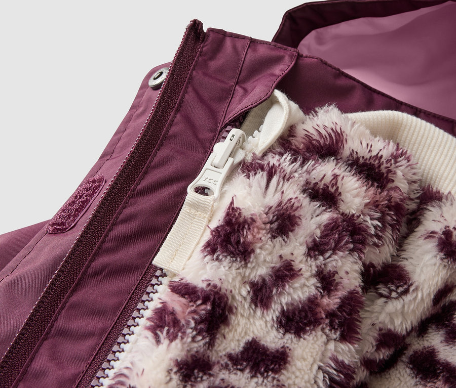 Gros plan sur une veste violet foncé, partiellement ouverte, révélant une couche intérieure moelleuse à imprimé léopard blanc et violet. La veste extérieure présente une fermeture éclair violet foncé et une bande velcro, avec une doublure rose plus claire visible à l'intérieur.