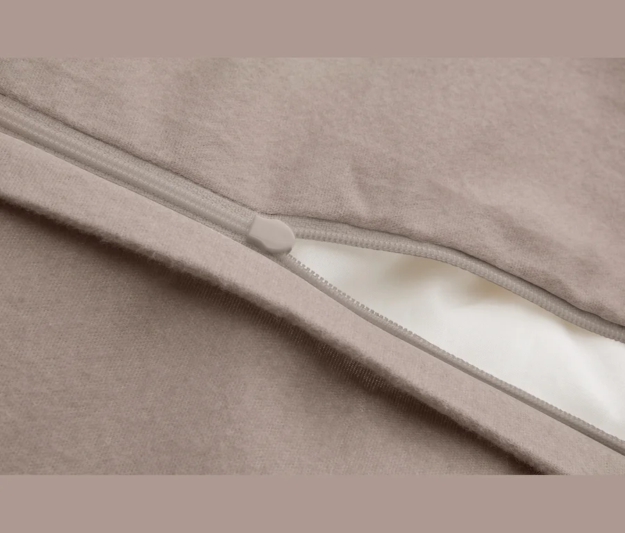 Gros plan d'un tissu beige avec une fermeture éclair gris clair partiellement ouverte, révélant une doublure blanche.