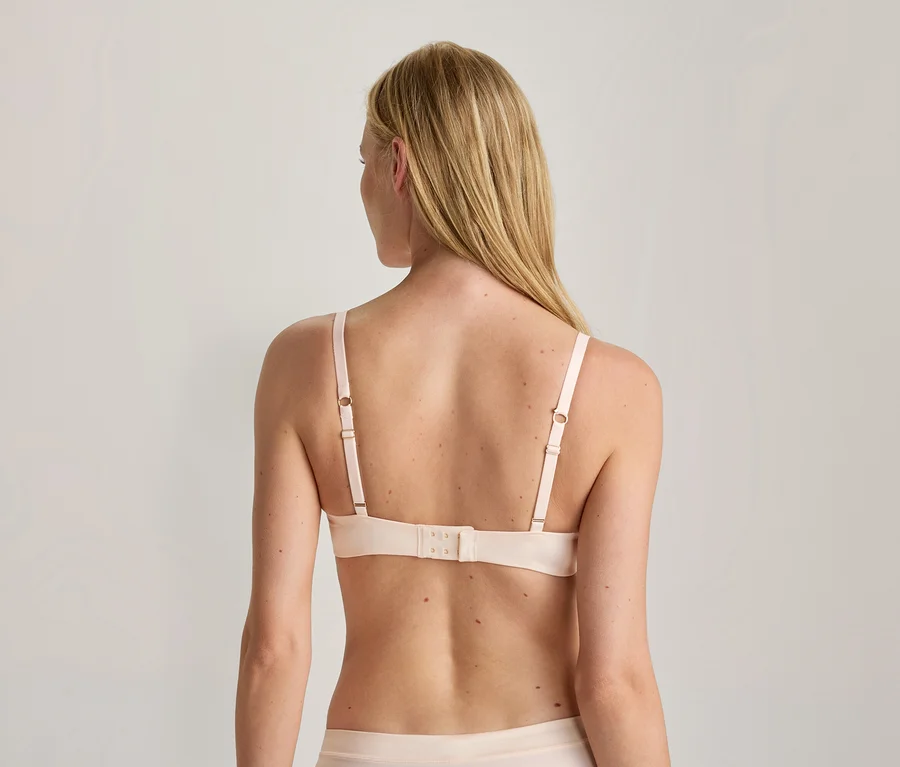 Dos d'une femme aux longs cheveux blonds, portant un soutien-gorge rose clair à bretelles réglables et une culotte assortie.