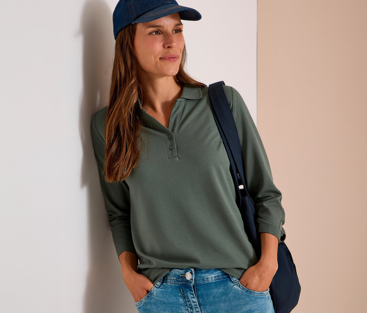 Femme en polo 3/4 vert CECIL, jean et casquette, appuyée contre un mur, mains dans les poches.