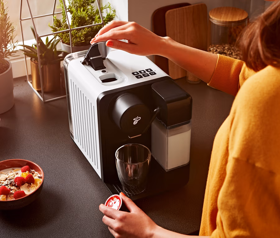 Une femme ouvre une machine à café Cafissimo milk blanche et tient une capsule.