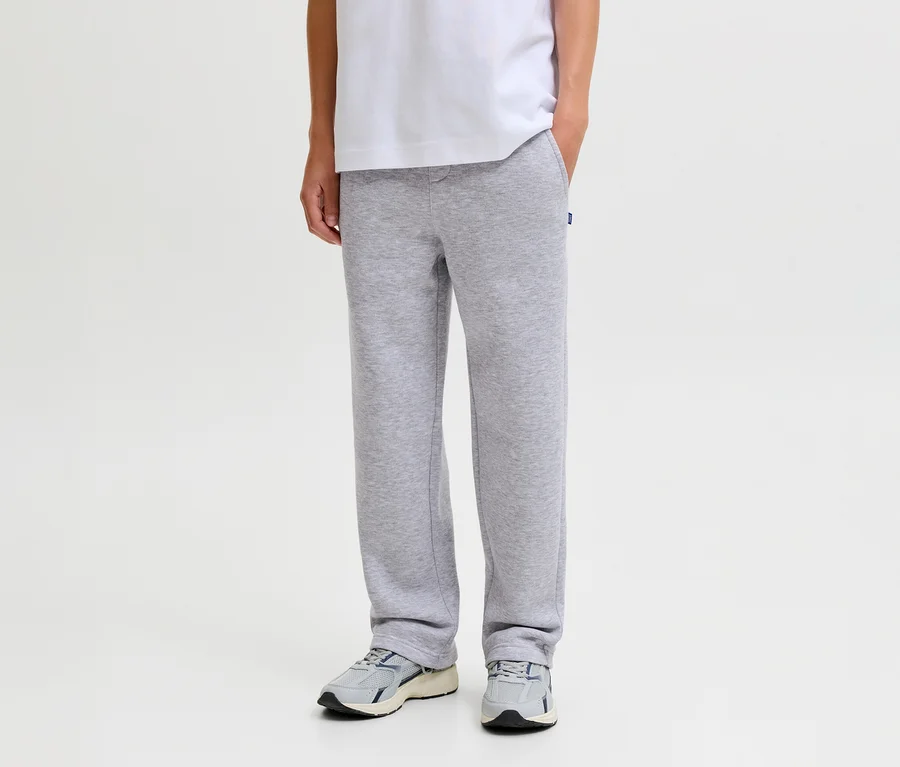 Personne portant un pantalon de survêtement gris Jack&Jones Bradley, un t-shirt blanc et des baskets grises, une main dans la poche.