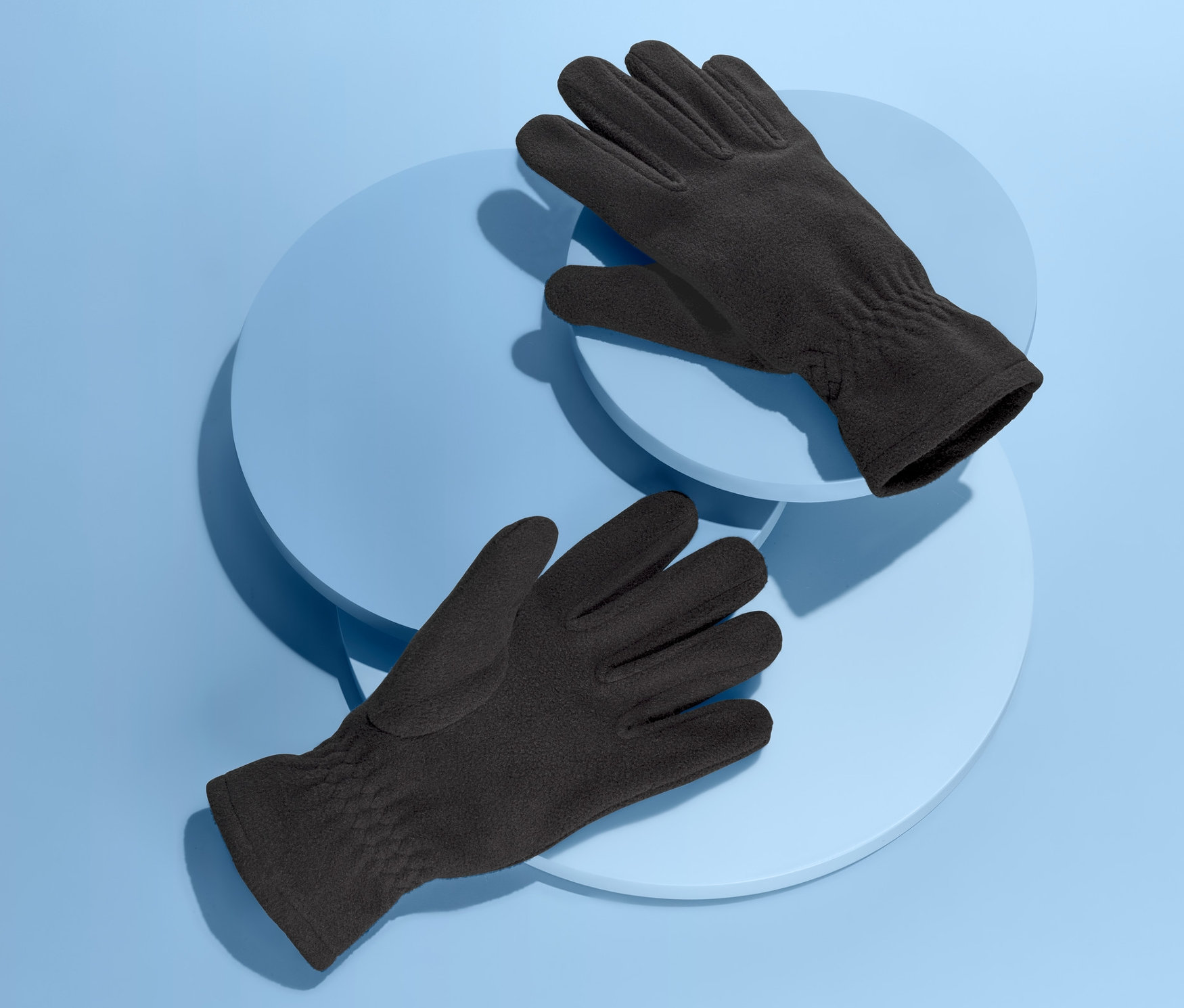 Deux gants en micropolaire reposent sur des plateformes circulaires bleu clair sur un fond bleu.