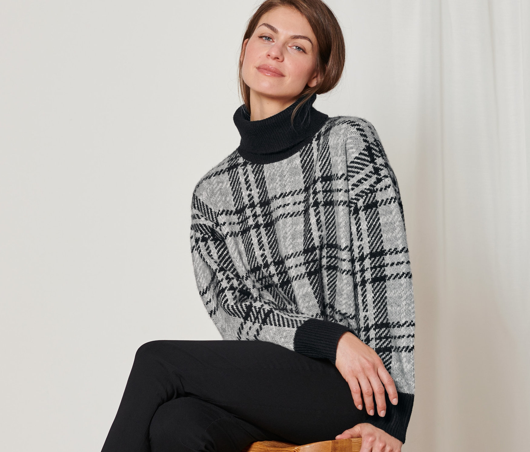 Femme assise sur un tabouret portant un pull en maille à col roulé.