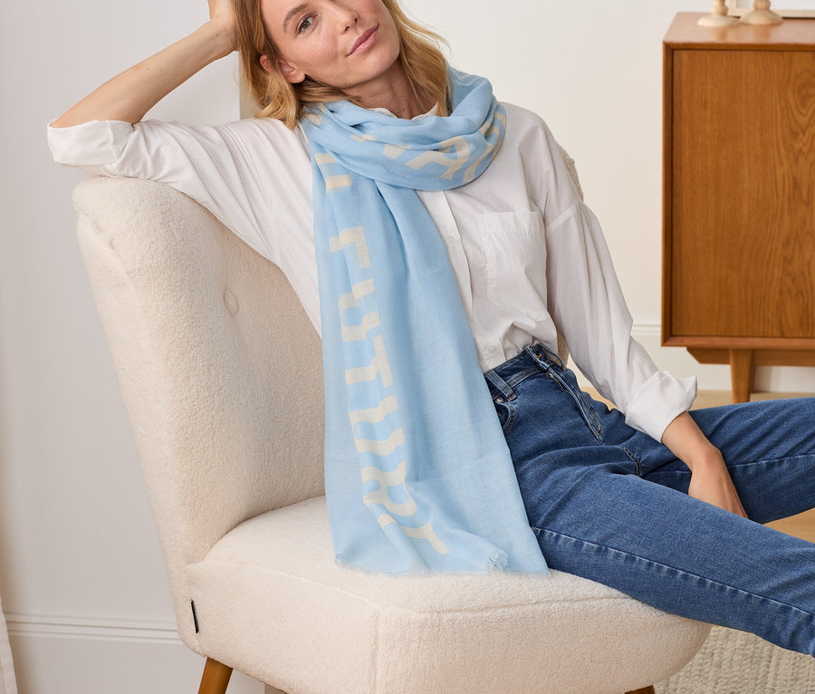 Femme assise dans un fauteuil portant une écharpe tissée avec inscription imprimée.