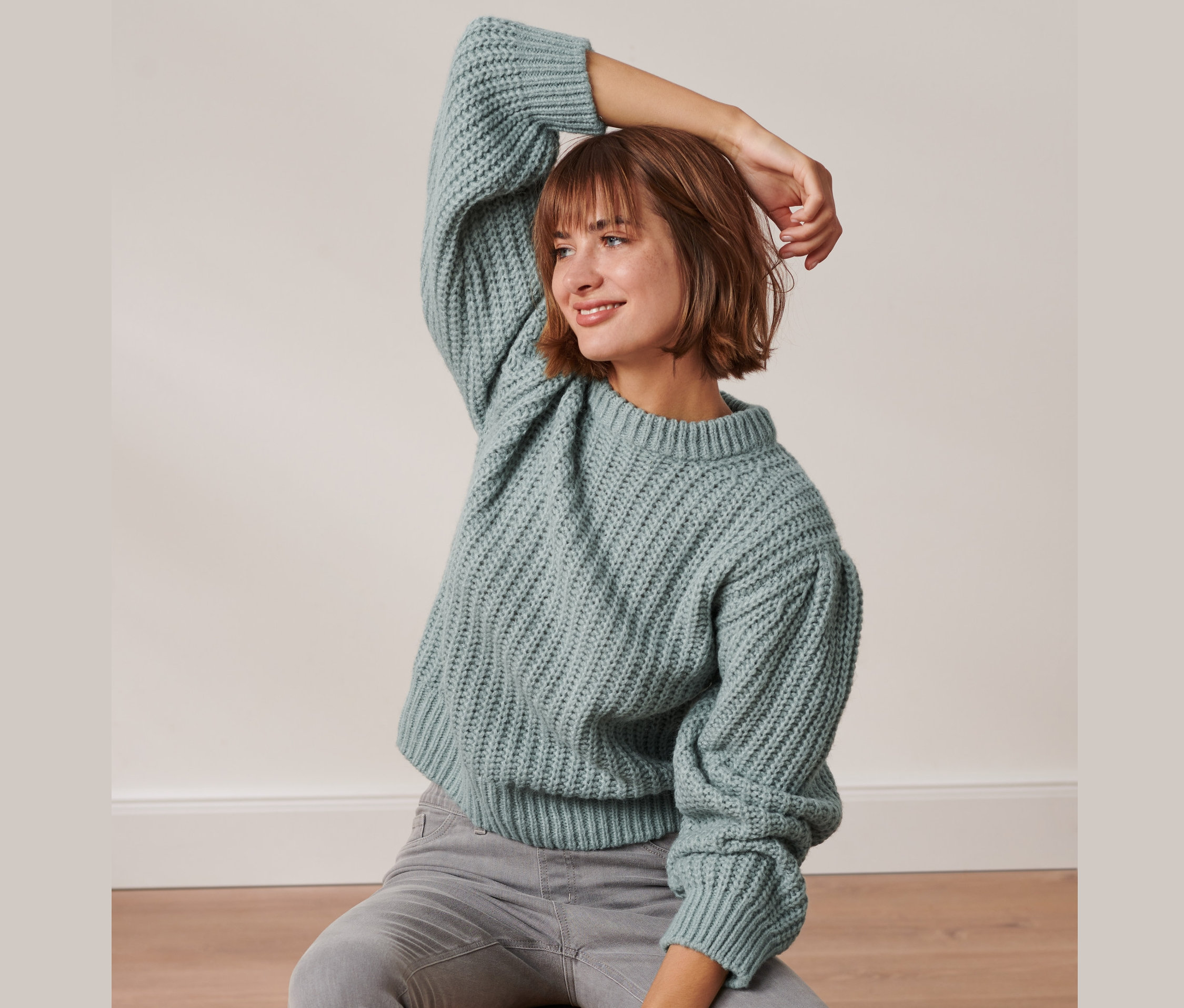 Femme assise posant dans un pull en grosse maille bleu fumée avec de la laine.