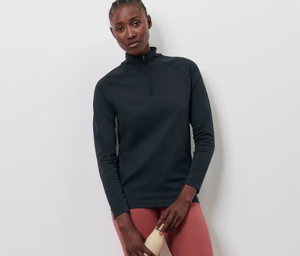 Femme posant en T-shirt d'entraînement sans coutures, leggings saumon et chaussures blanches, tenant une bouteille d'eau.