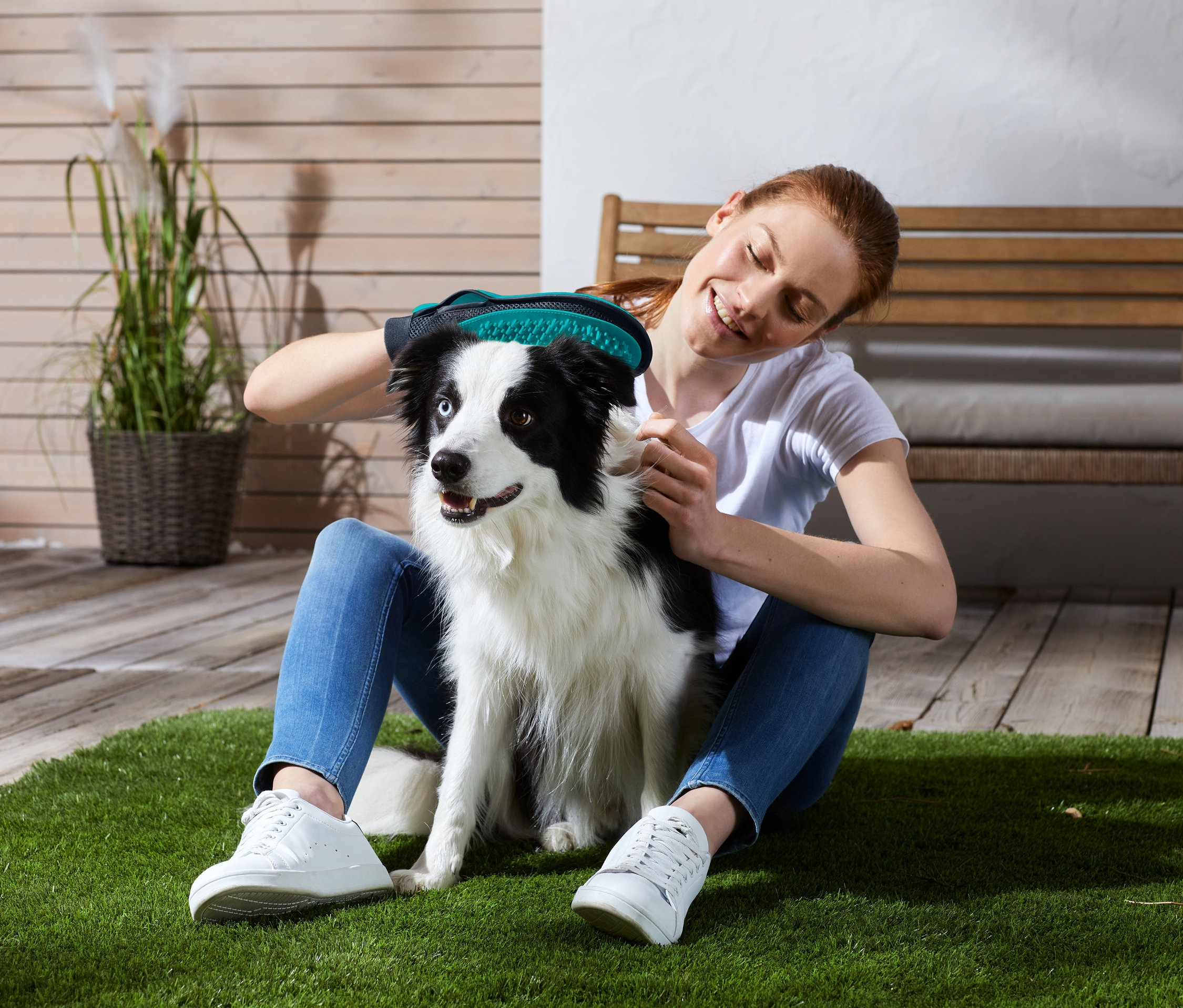 Une femme assise sur l'herbe utilise un gant de soin du pelage 2 en 1 sur un chien.