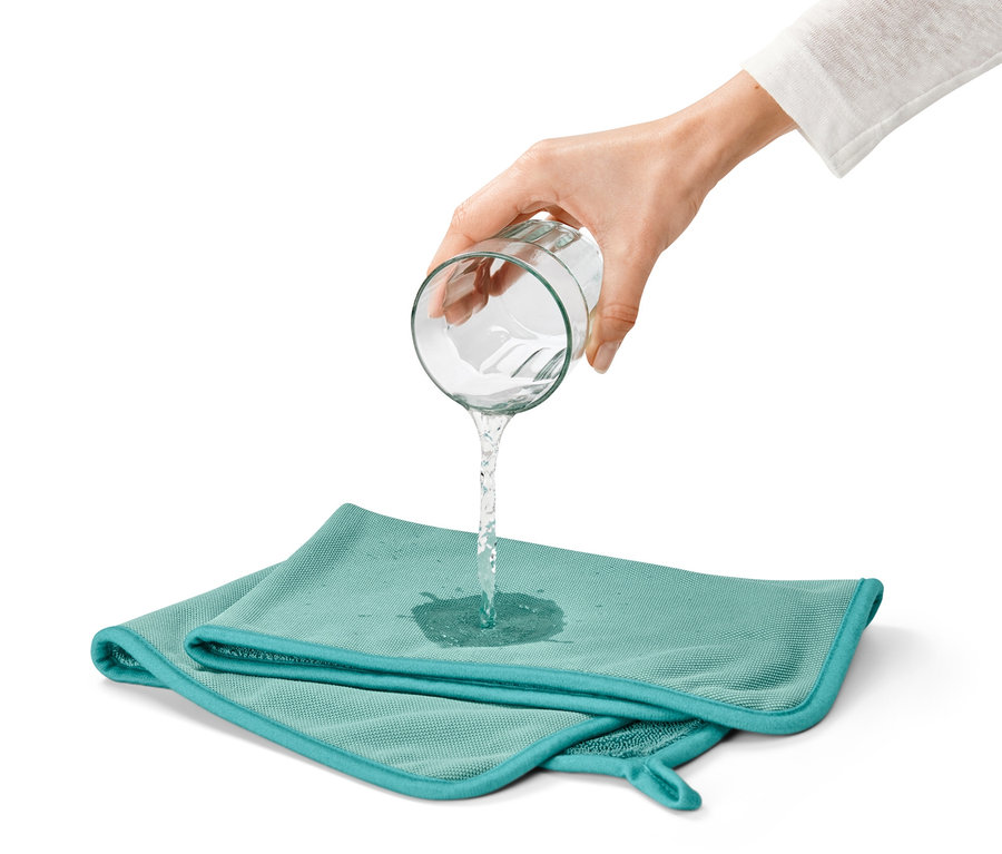 Une main verse de l'eau d'un verre sur un chiffon sec très absorbant bleu-vert.