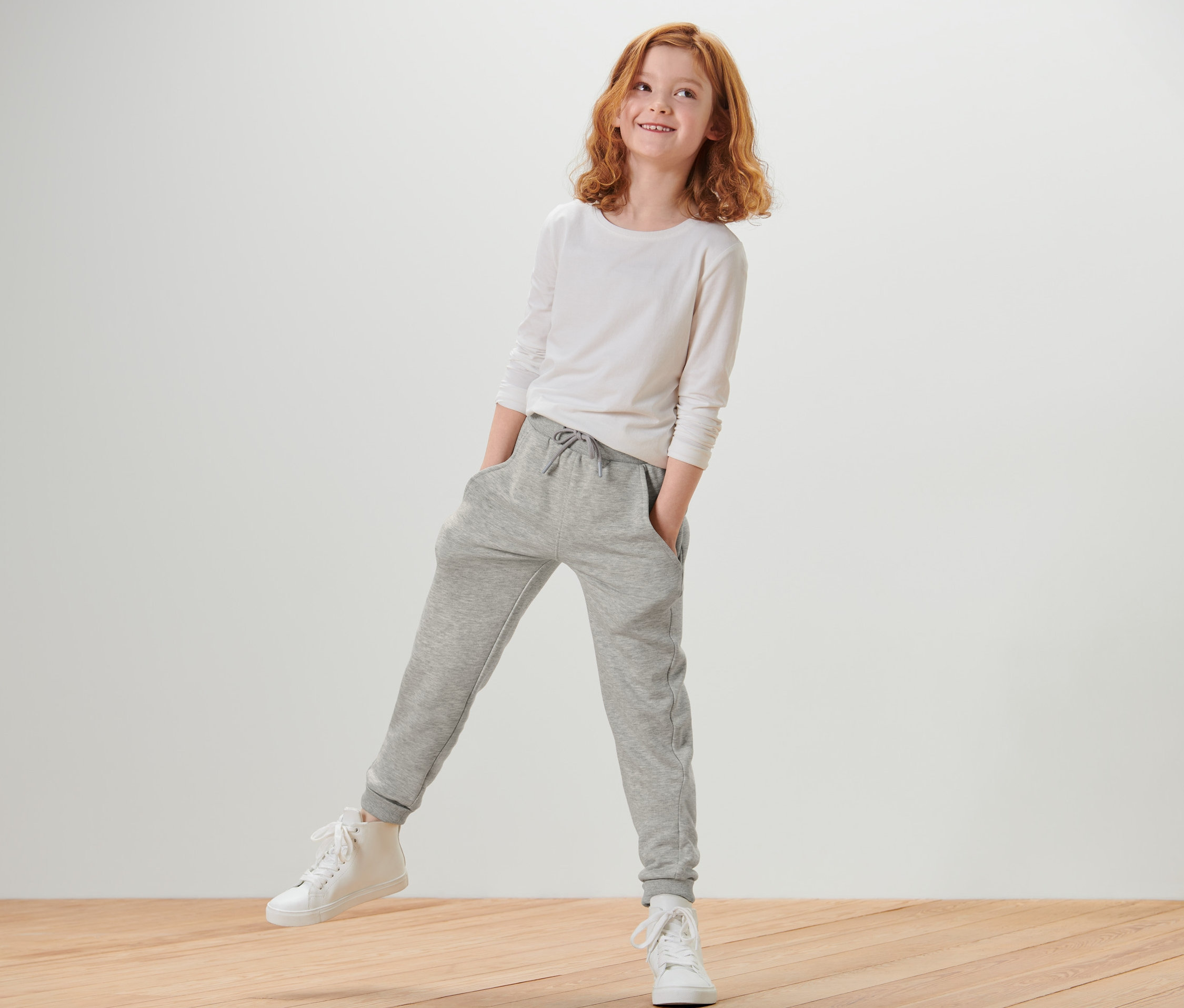 Fillette portant un t-shirt à manches longues blanc et un pantalon de survêtement gris chiné.