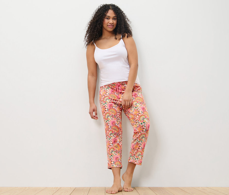 Une femme appuyée contre un mur porte un pantalon de pyjama et un débardeur.