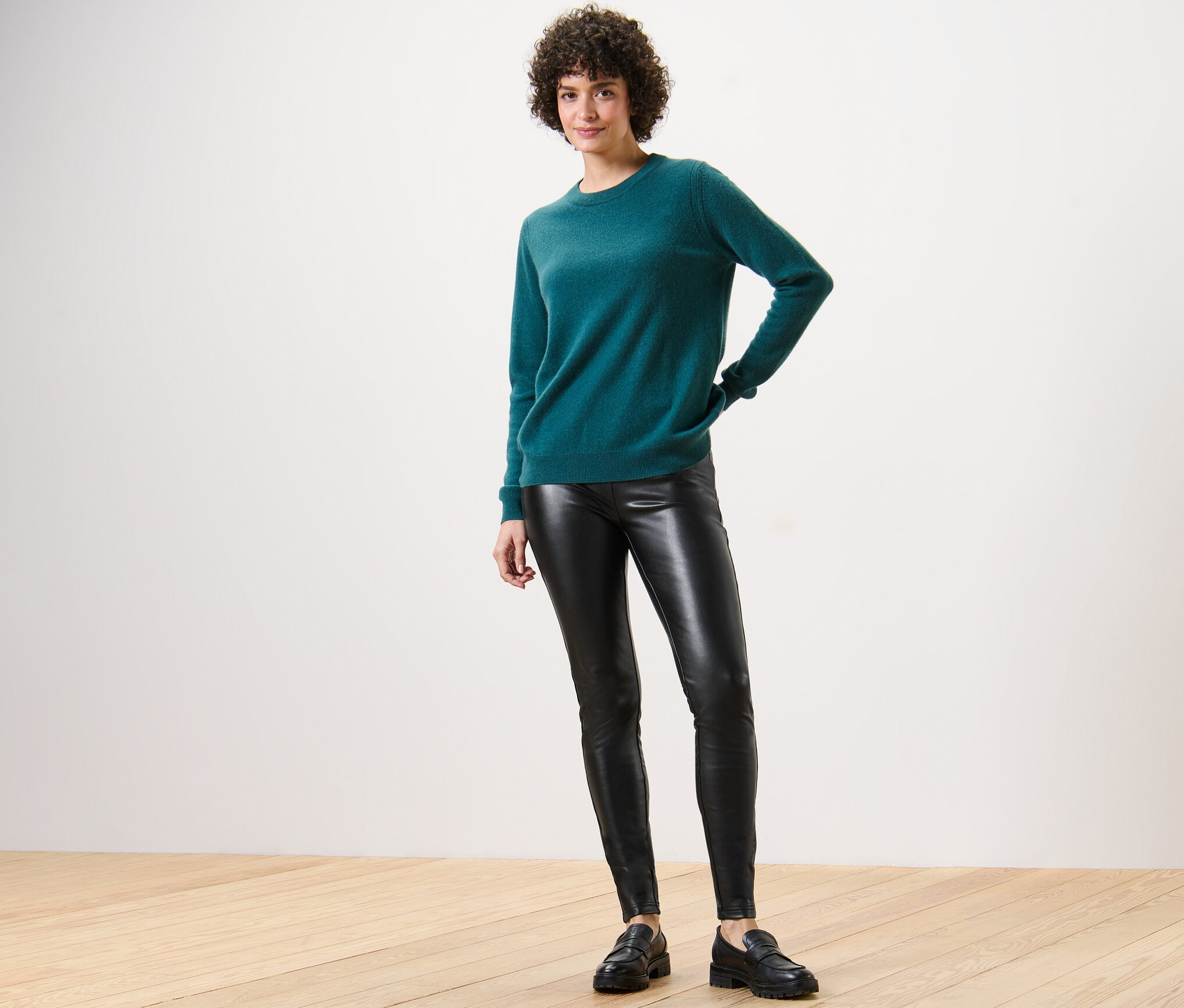 Femme posant en pull vert et legging aspect cuir.