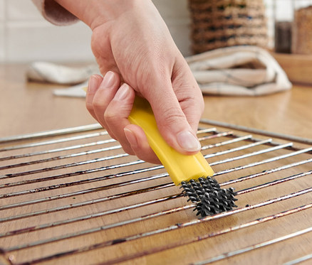 Femme nettoyant une grille de four avec une brosse à four avec racloir.