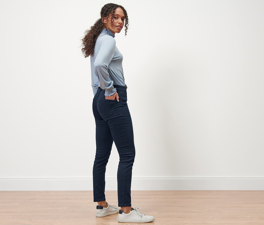 Une femme se tient de côté et pose en portant des treggings bleu foncé coupe « Nelly ».