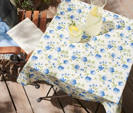 Sur une table sur une terrasse se trouve une nappe lavable d'environ 90 x 90 cm avec des fleurs bleues.