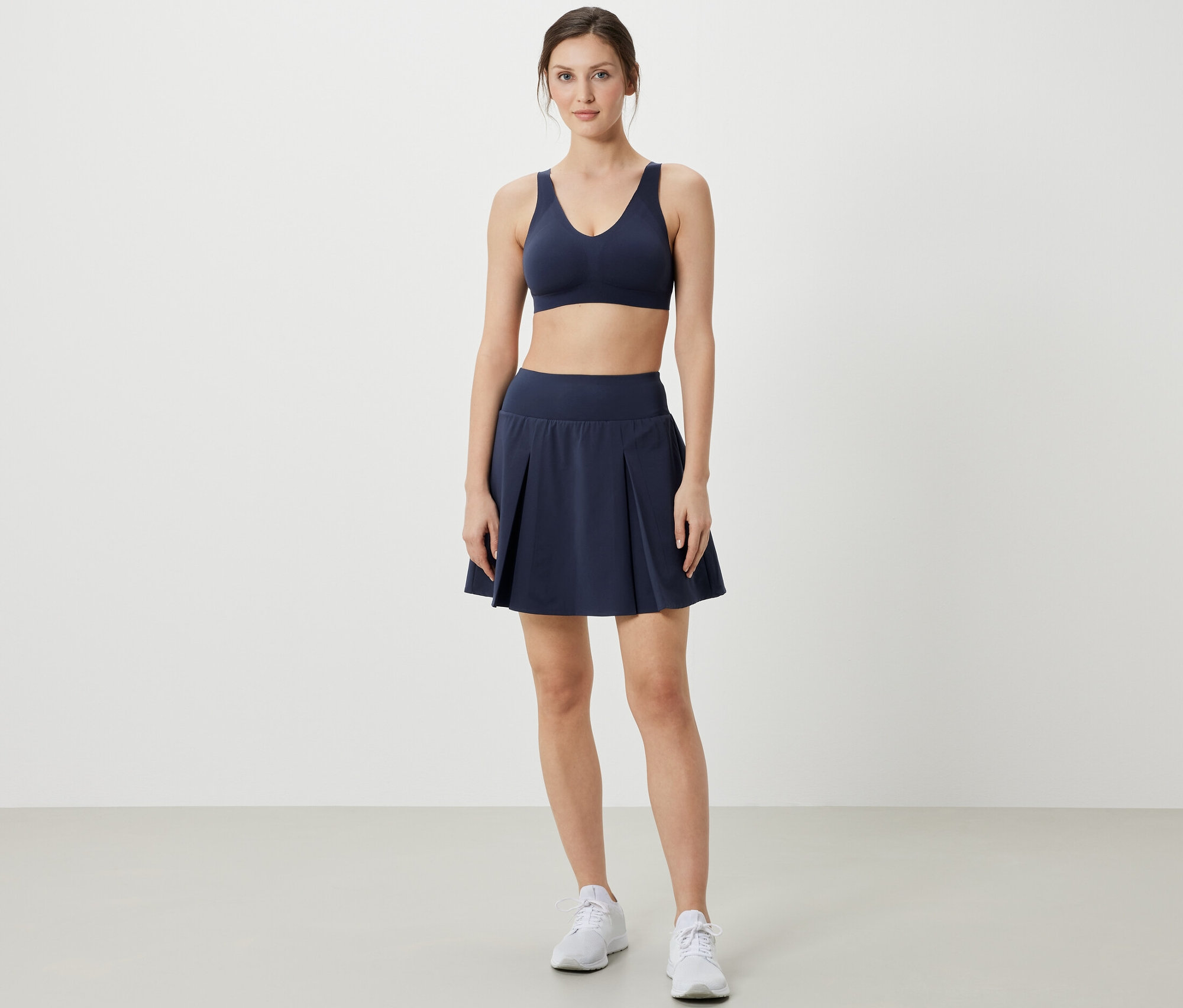 Femme posant en soutien-gorge de sport et jupe de sport bleu foncé.