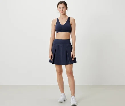 Femme posant en soutien-gorge de sport et jupe de sport bleu foncé.