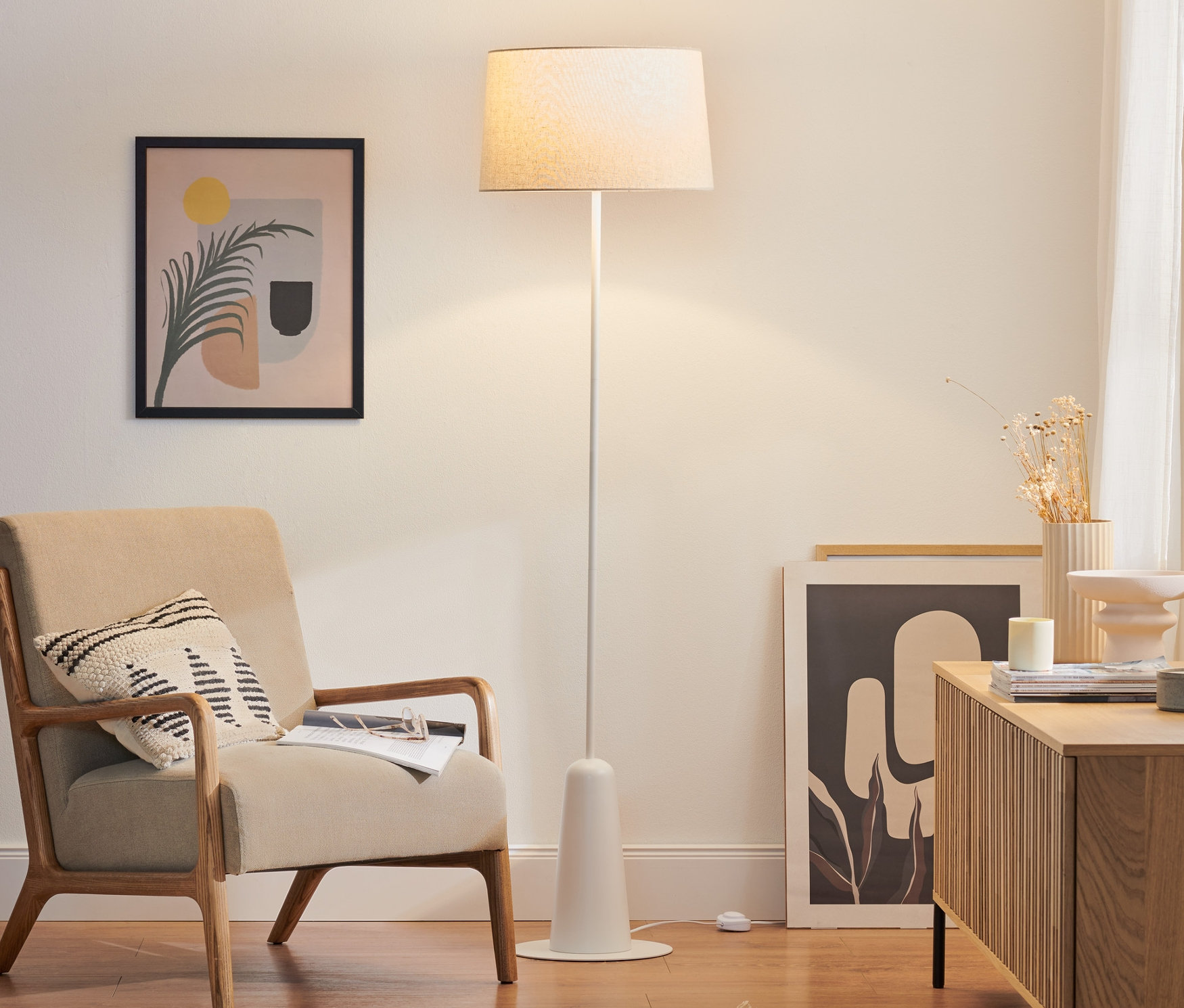 Un lampadaire blanc avec abat-jour textile se trouve dans le salon à côté d'un fauteuil beige.