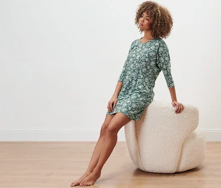 Femme assise sur un fauteuil et portant une chemise de nuit pétrole avec imprimé intégral.