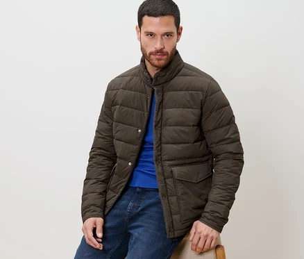 Un homme est assis et porte une veste matelassée, un jean bleu et un t-shirt bleu.