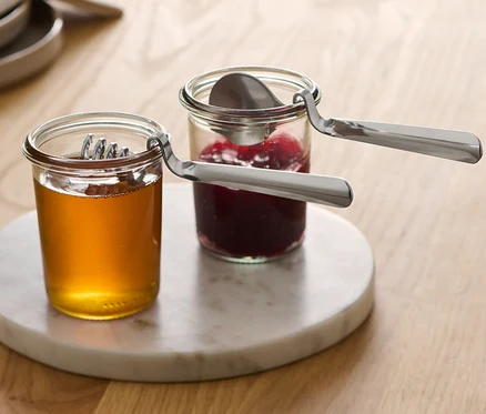 Deux pots de confiture et de miel sont posés sur un plateau en marbre, chacun contenant une cuillère à confiture et à miel.