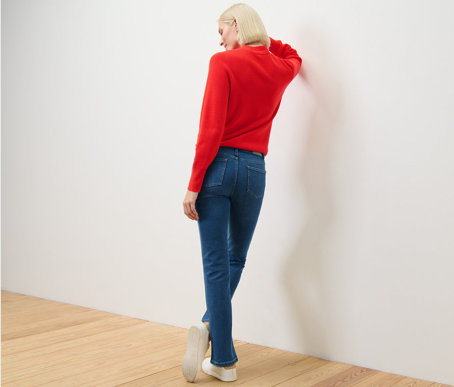 Femme portant un pull rouge et un jean droit – Fit « Kira » appuyée contre le mur.