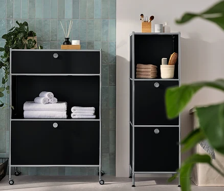 Une commode étroite en métal « CN3 » avec 2 compartiments à abattants et une commode métallique « CN3 » avec 1 tiroir et 1 compartiment à abattant sont dans la salle de bain. Des serviettes et des accessoires sont posés sur les commodes.