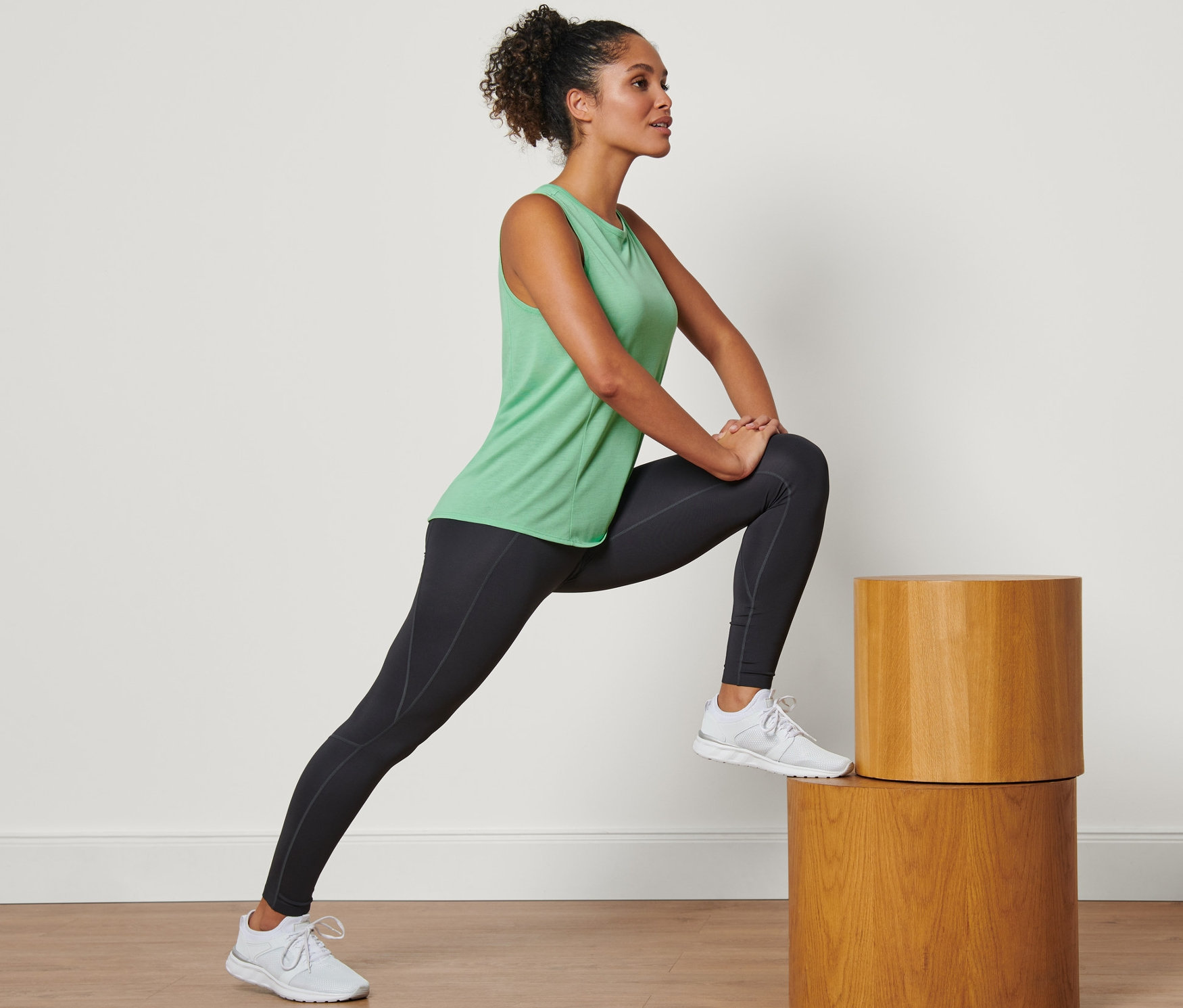 Femme s'étirant sur des marches en bois et portant un débardeur de sport vert.
