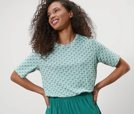 Femme posant en chemise en interlock à motif coquillage et pantalon vert.