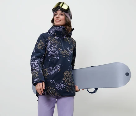 Femme tenant un snowboard et portant une veste de ski à fermeture demi-zippée.