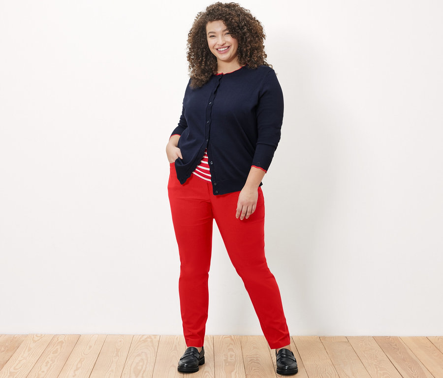 Femme posant en pantalon rouge en bengaline, un t-shirt rayé et un cardigan à maille fine avec bord ondulé.