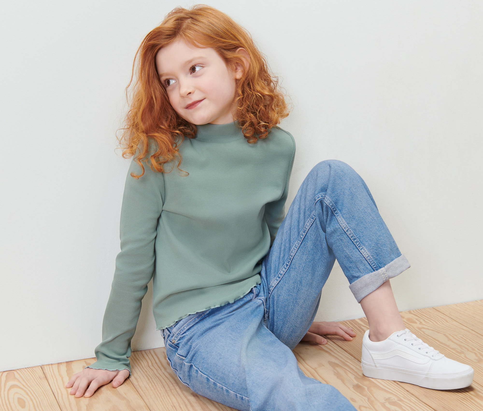 Une fille assise par terre porte un t-shirt manches longues vert et un tregging pour enfant – Fit « Jule ».