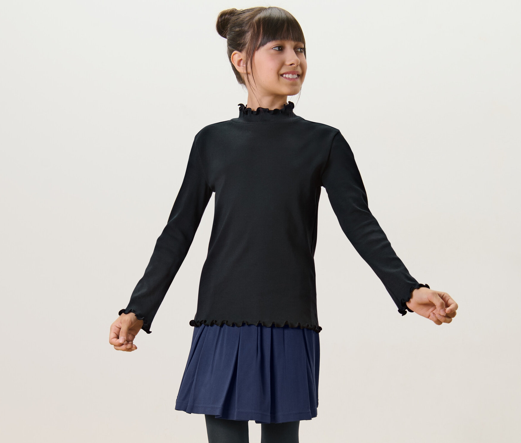 Une fille porte un T-shirt manches longues enfant noir et une jupe bleue.