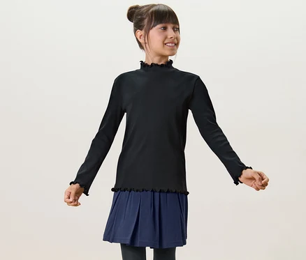 Une fille porte un T-shirt manches longues enfant noir et une jupe bleue.