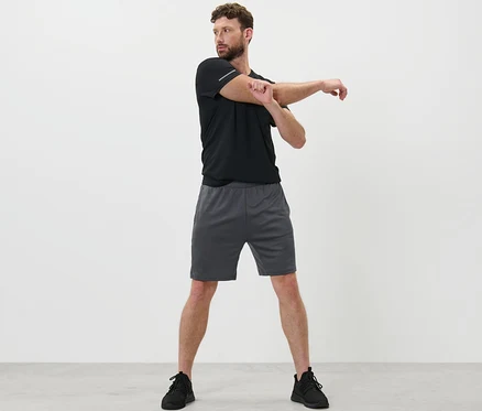 Homme étirant le bras en short de sport.