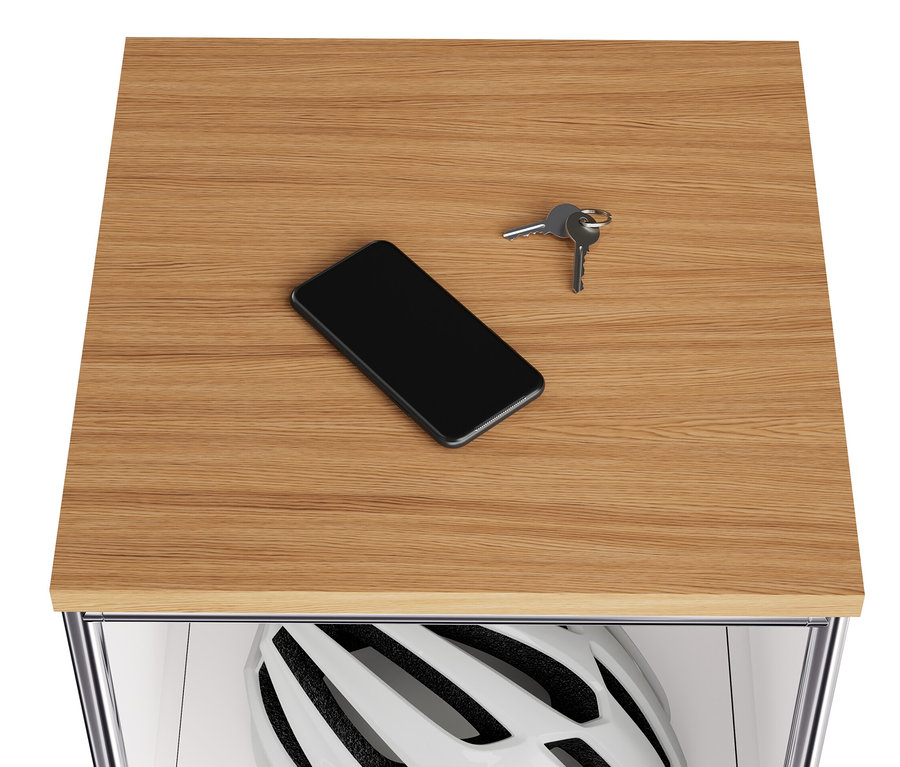 Sur le plateau en bois d'une commode étroite en métal blanc « CN3 », reposent un téléphone portable et des clés. Un casque se trouve dans le compartiment rabattable.