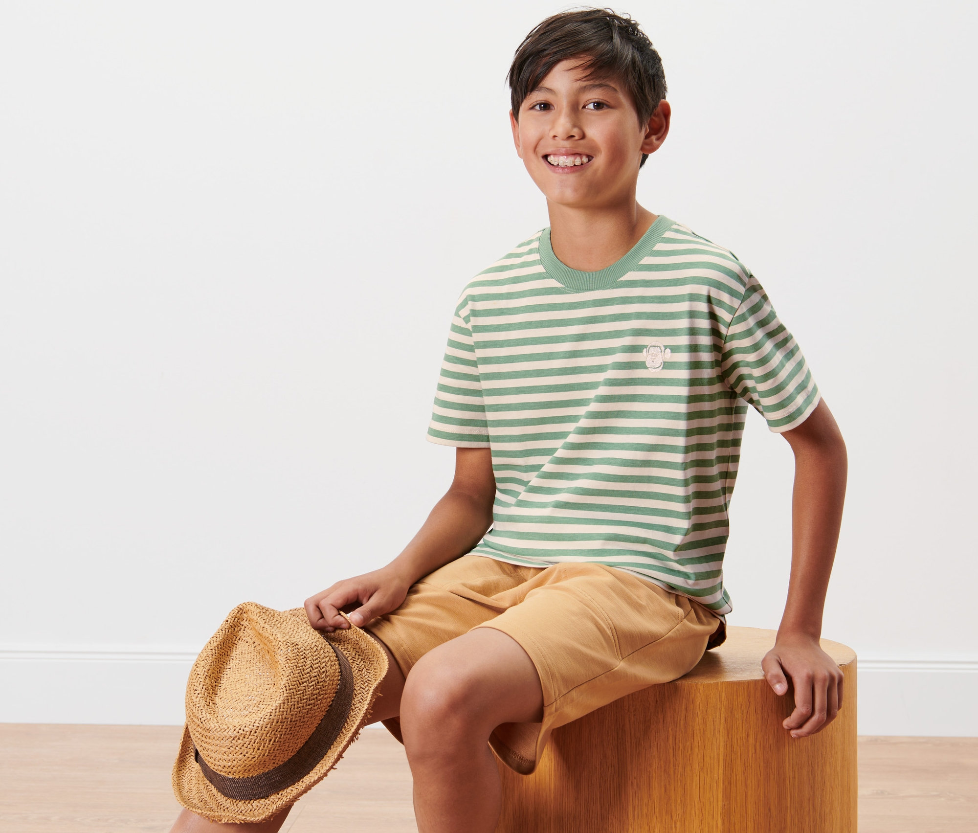 Un garçon est assis et tient un chapeau. Il porte 2 t-shirts pour enfant.