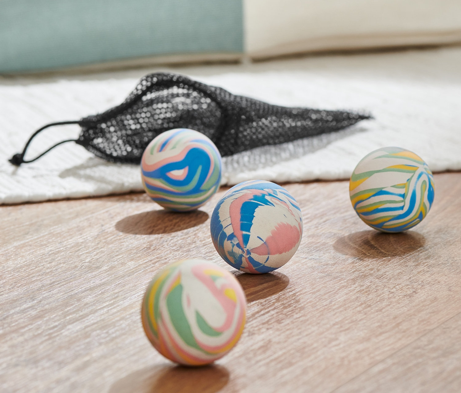 Quatre balles rebondissantes multicolores et un sac en filet noir sur un plancher en bois.