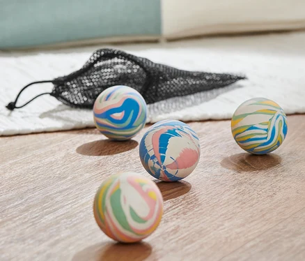 Quatre balles rebondissantes multicolores et un sac en filet noir sur un plancher en bois.