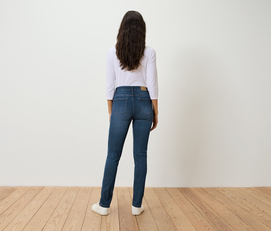 Une femme se tient dos à la caméra et porte un jean bleu, une chemise blanche à manches trois-quarts et des baskets blanches.