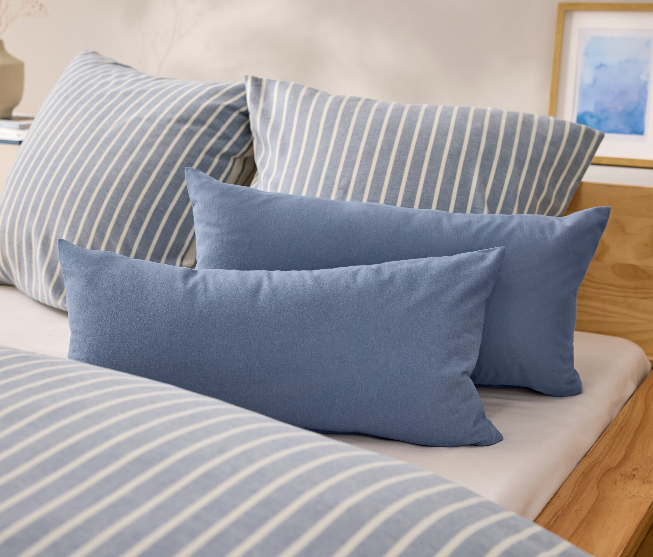 Sur un lit, il y a deux oreillers rectangulaires bleus et deux oreillers à rayures bleues et blanches.