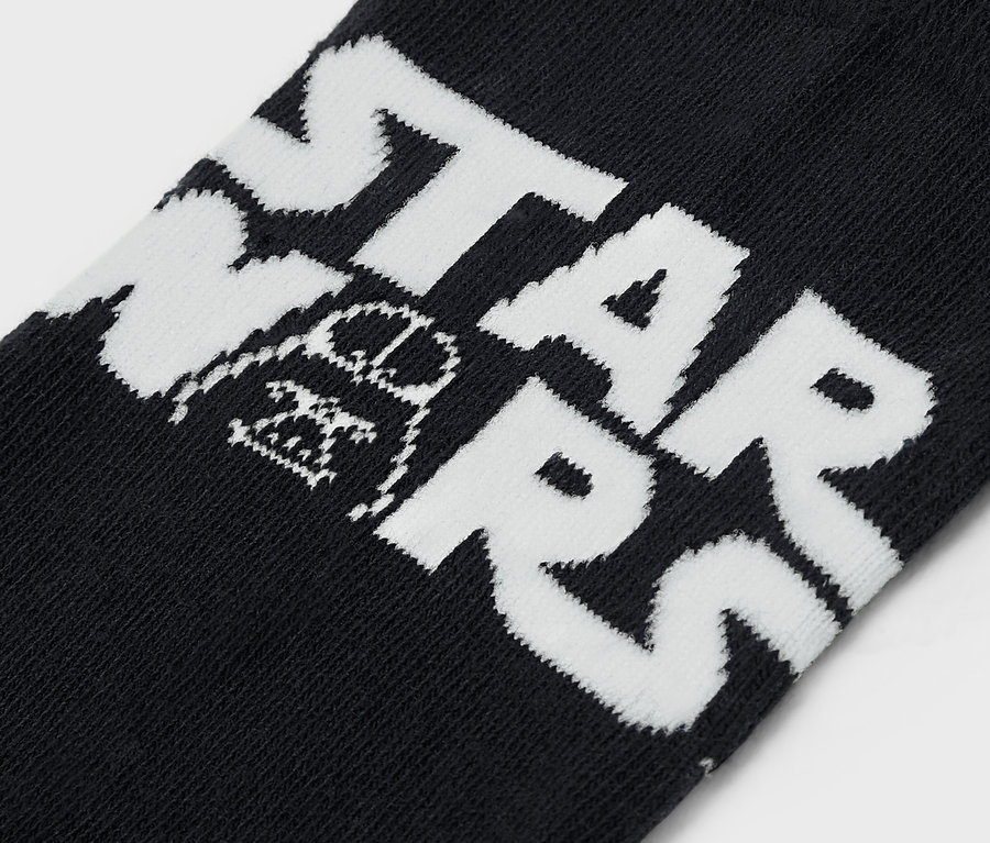 Détail d'une chaussette noire avec l'inscription blanche STAR WARS et une illustration de Darth Vader.