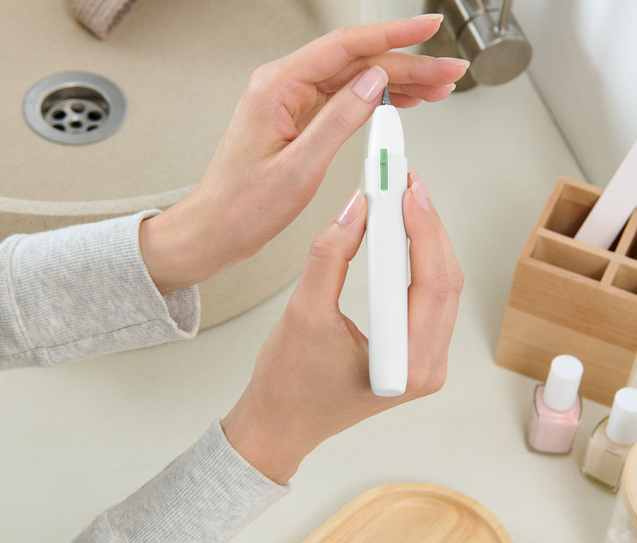 Une femme tient une fraise à ongles blanche devant un lavabo.