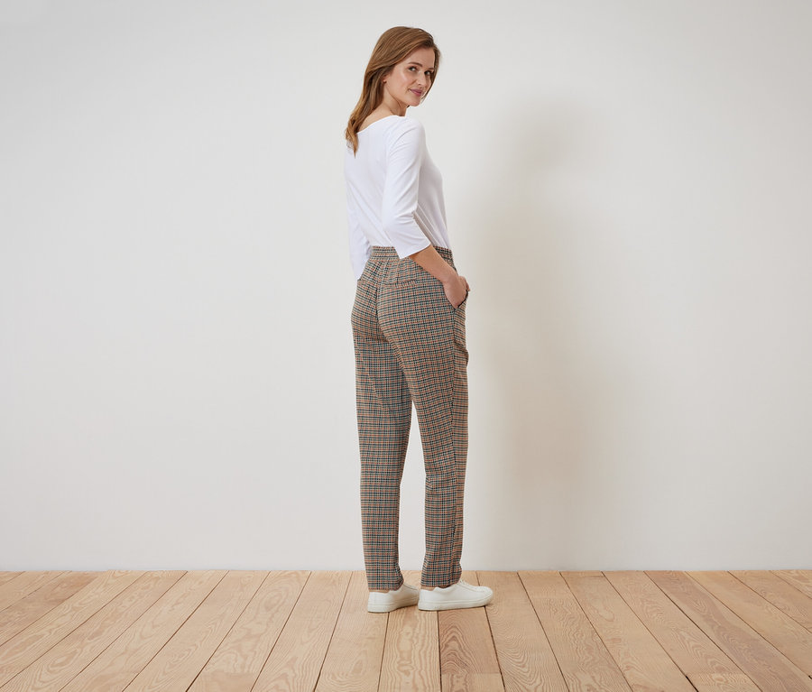 Femme posant en pantalon à carreaux et haut blanc.