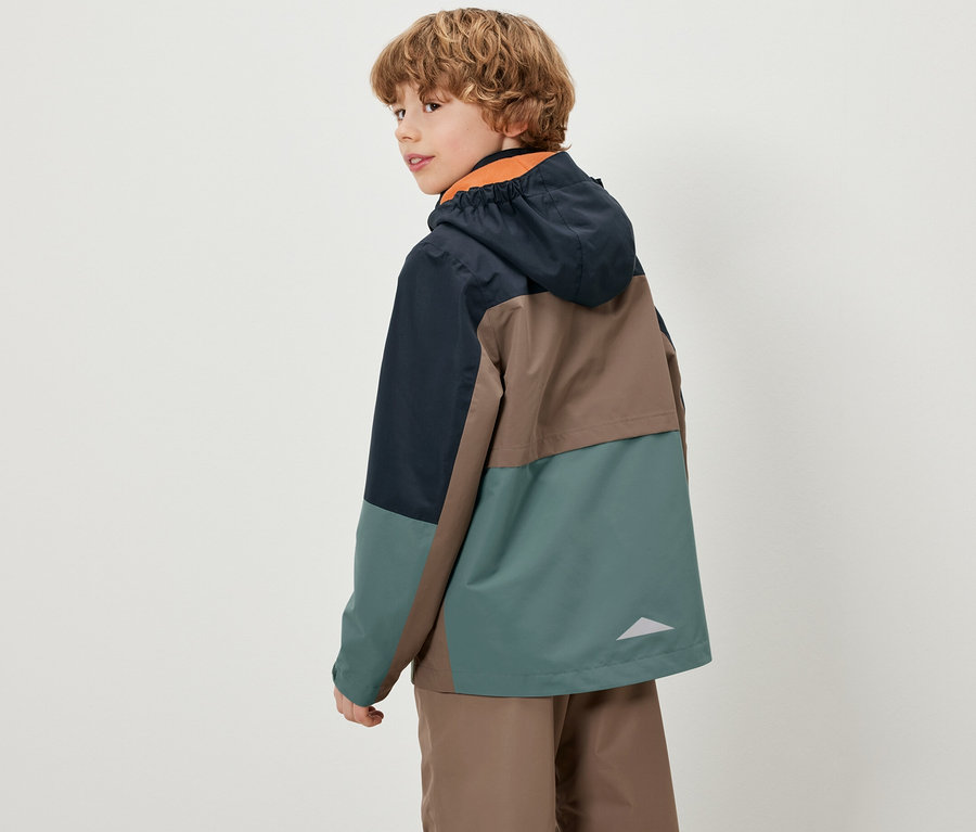 Un garçon regarde par-dessus son épaule et porte une veste colorée pour enfants tout temps.