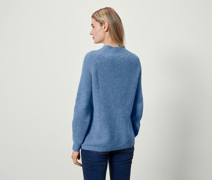 Une femme blonde, vue de dos, porte un pull bleu et un jean.